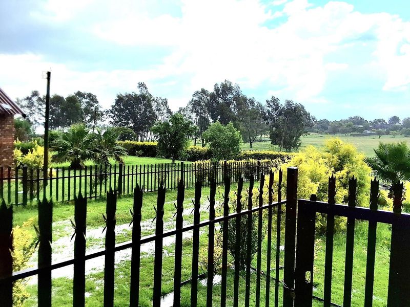 A view of a spacious garden featuring a well-maintained lawn, mature trees, and secure metal perimeter fencing with a gated entrance.