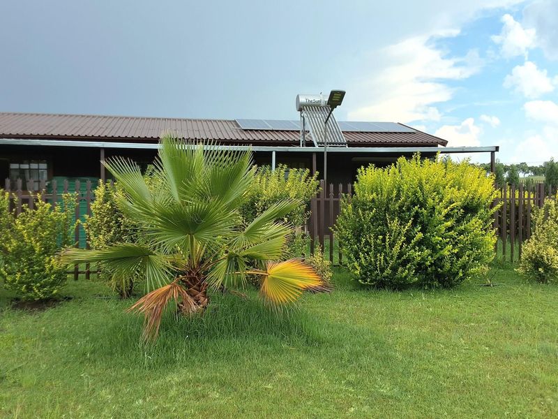 Rear view of the property featuring a metal roof, solar water heating system, solar panels, and a well-maintained garden with a picket fence.
