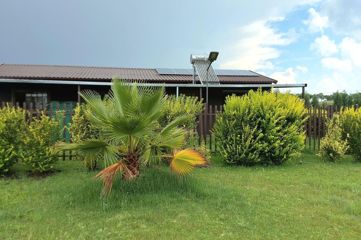 Rear view of the property featuring a metal roof, solar water heating system, solar panels, and a well-maintained garden with a picket fence.