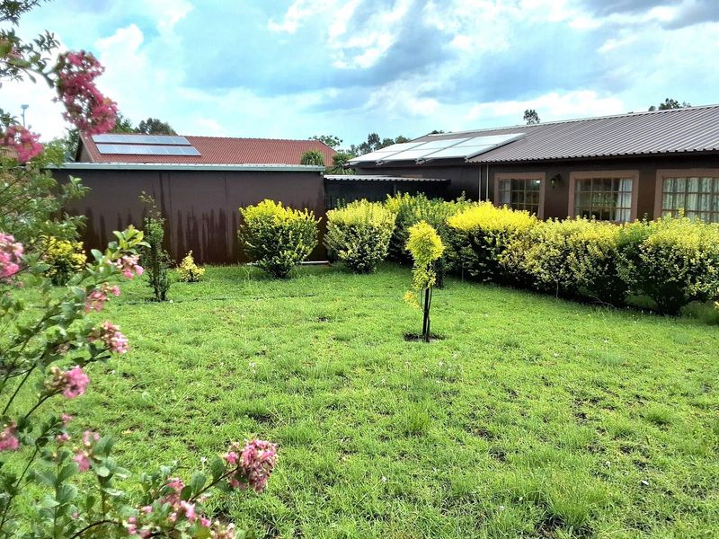 A well-maintained rear garden featuring a lawn, established shrubs, and a house exterior equipped with solar panels on a metal roof.