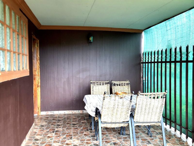 A covered patio area featuring tiled flooring, timber wall cladding, and a secure metal perimeter fence, providing a functional outdoor entertainment space.