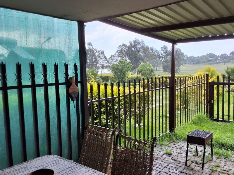 A covered outdoor patio area featuring brick paving and metal fencing, offering views of the surrounding garden and landscape.