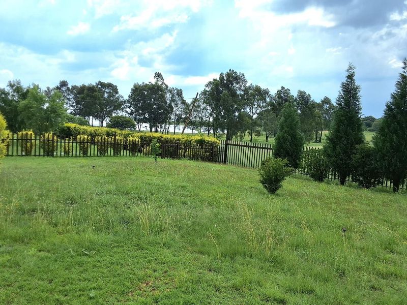 A spacious, well-maintained garden area featuring a metal perimeter fence and established trees, offering a peaceful outdoor setting.
