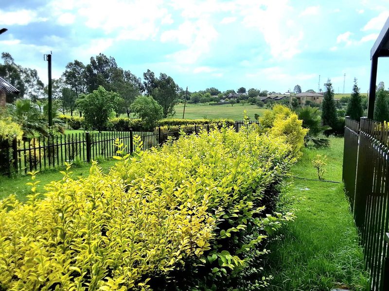 A well-maintained garden area featuring manicured hedges, metal perimeter fencing, and outdoor lighting, overlooking a scenic neighborhood landscape.