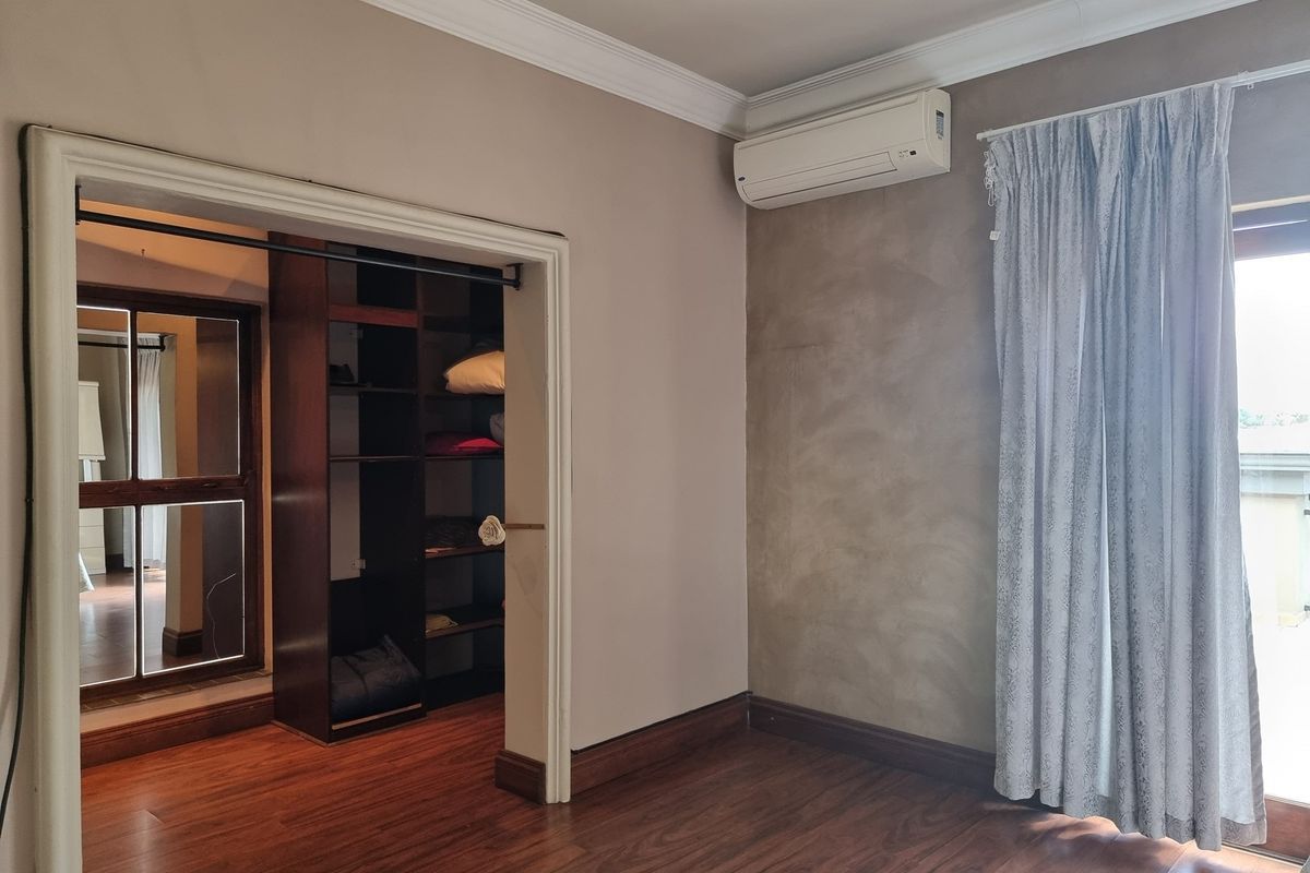 A bedroom featuring laminate flooring, crown molding, a built-in wardrobe, and a wall-mounted air conditioning unit.