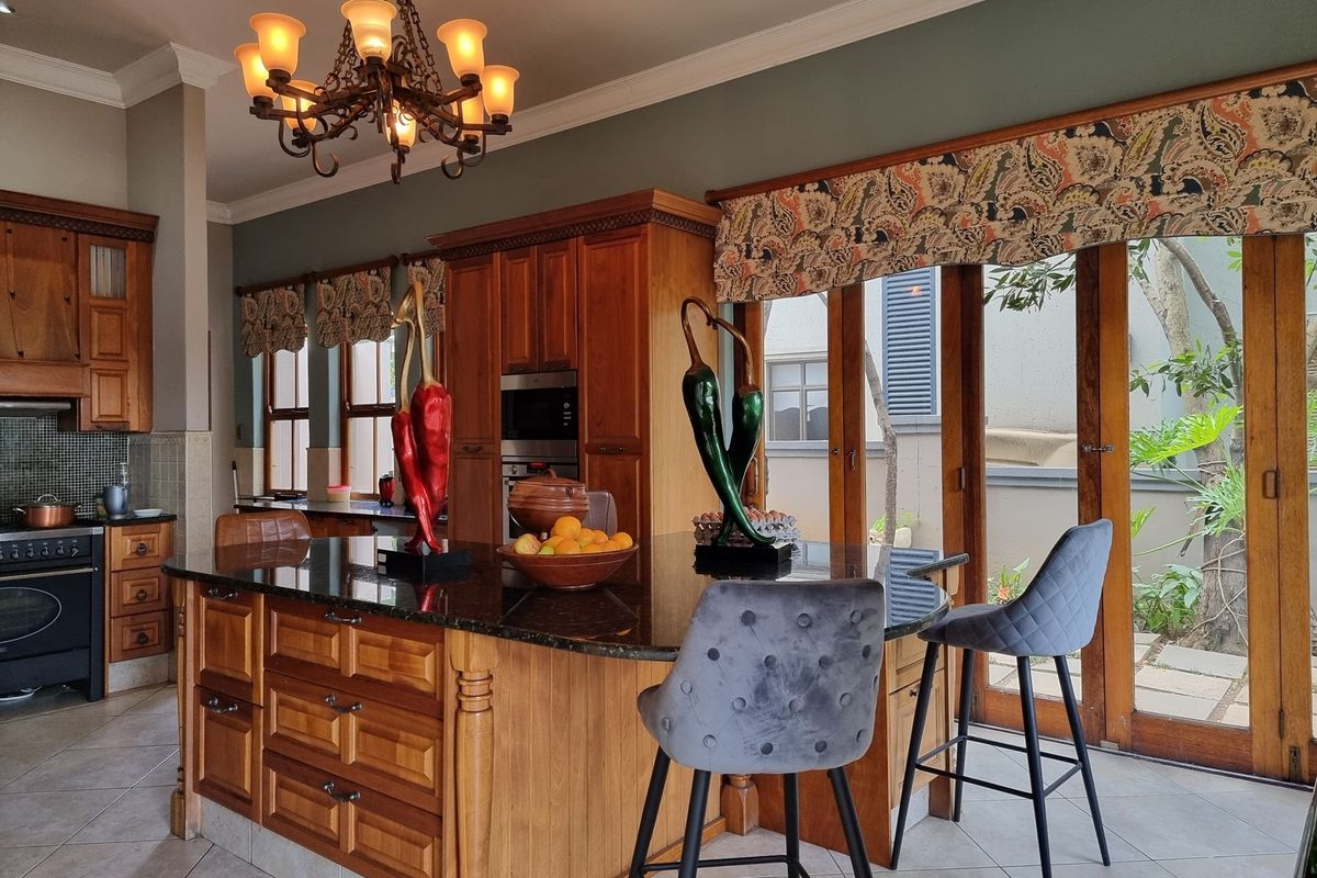 Spacious kitchen featuring warm wooden cabinetry, a large granite-topped island, built-in appliances, and direct access to the outdoor area through wooden folding doors.