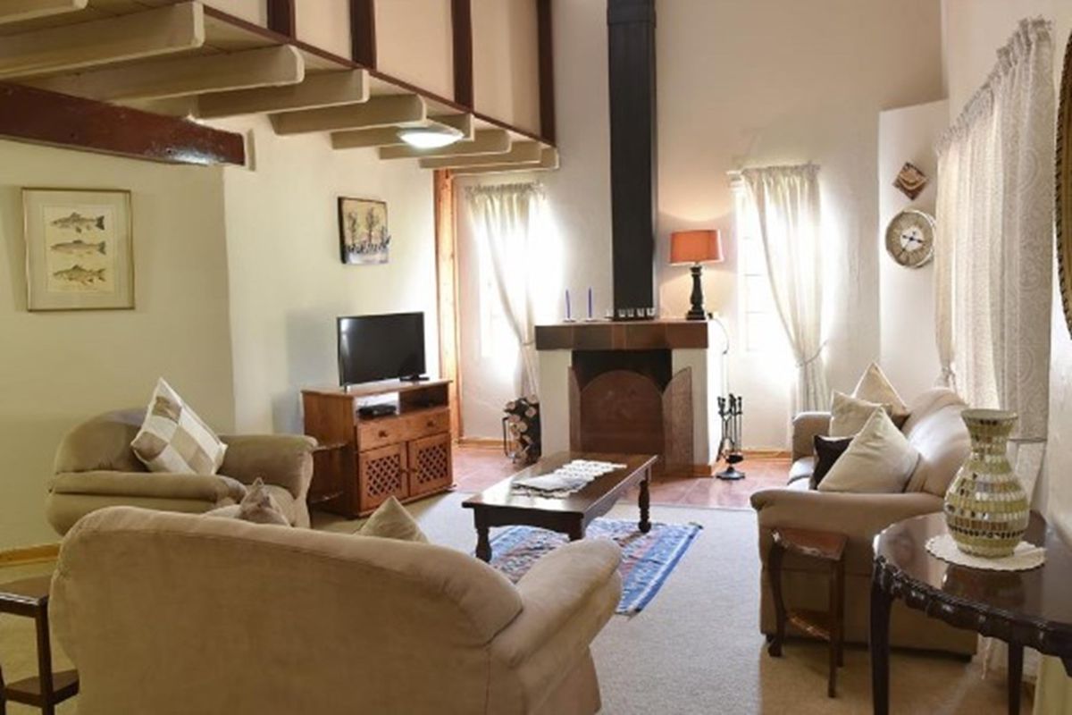 Cozy living room featuring a prominent fireplace, exposed timber ceiling beams, and a mezzanine level, creating a warm and inviting atmosphere.