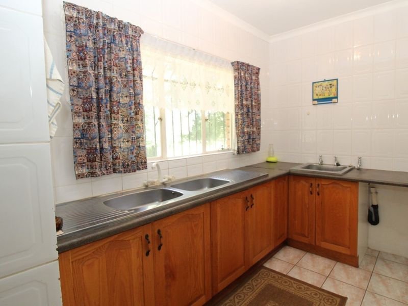 A functional kitchen featuring wooden cabinetry, double stainless steel sink, tiled walls, and a window with security bars.