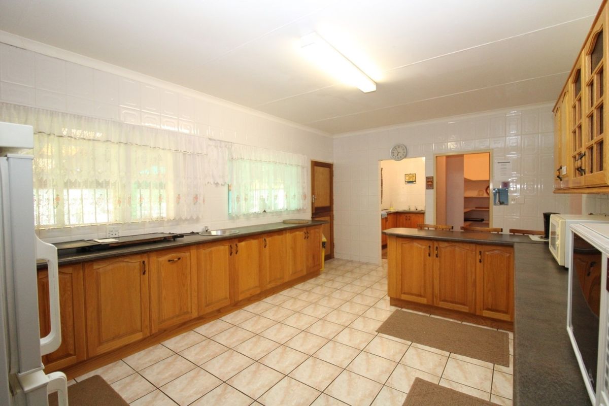 A functional kitchen featuring wooden cabinetry, tiled walls, and tiled flooring, with an adjacent scullery area visible through the doorway.