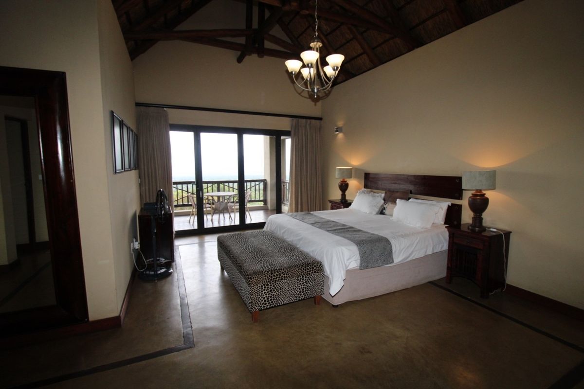 Spacious bedroom featuring a high vaulted thatched ceiling, polished concrete flooring, and large sliding glass doors opening onto a private balcony.