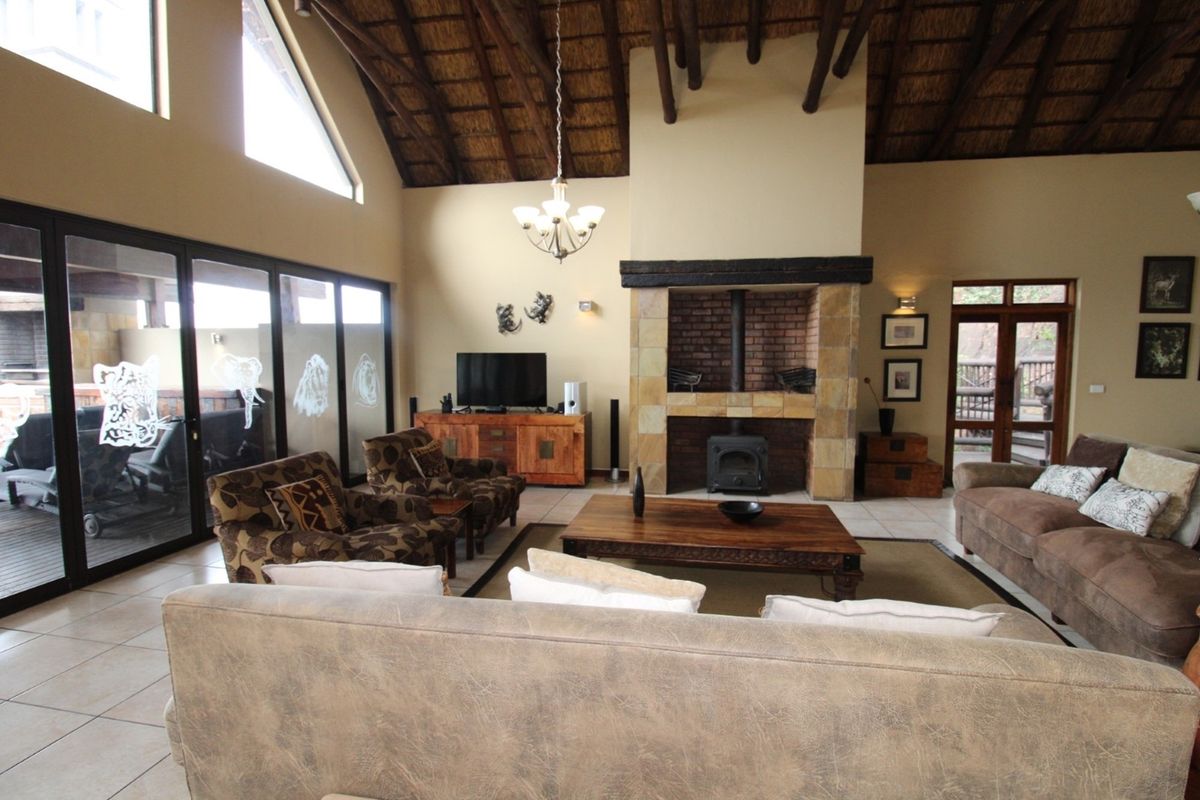 Spacious living room featuring a high vaulted thatched ceiling, exposed timber beams, and a prominent stone-clad fireplace with a built-in wood-burning stove.