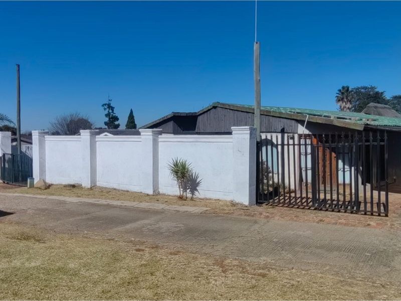 Street view of the property featuring a white perimeter wall, metal security gate, and a pitched roof structure.