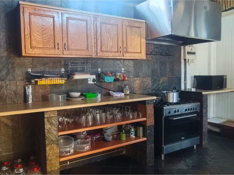A functional kitchen area featuring dark stone wall tiling, wooden cabinetry, a freestanding stove with a stainless steel extractor hood, and open shelving.