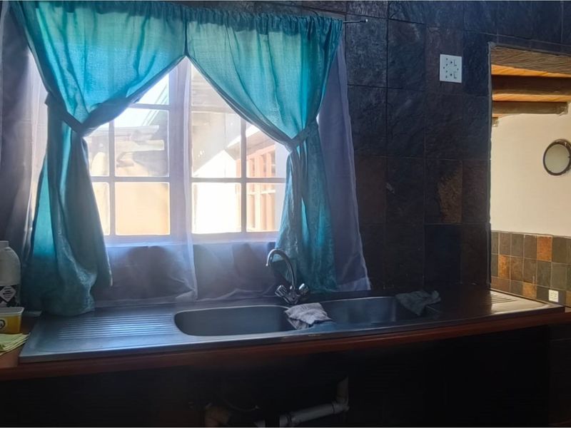 A kitchen sink area featuring a double basin, dark stone-style wall tiling, and a window with natural light.