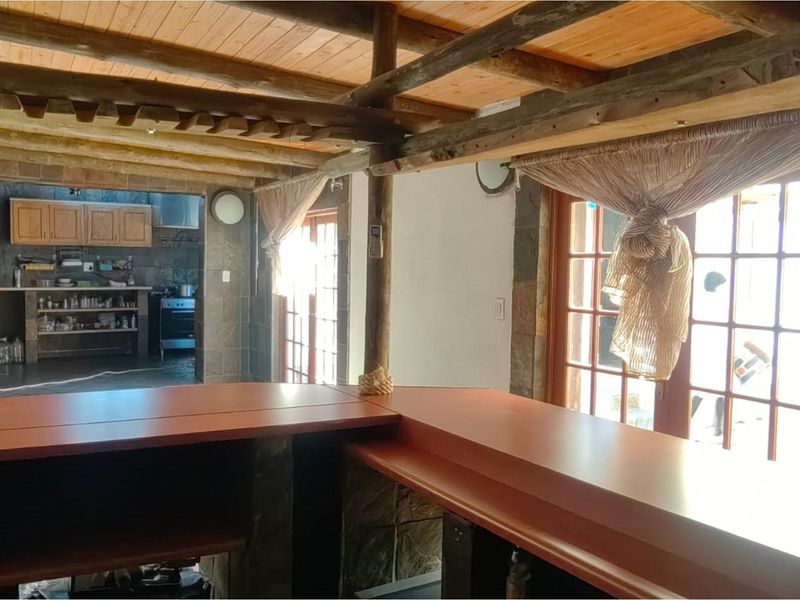 Open plan living area featuring a built-in bar counter, exposed timber beam ceiling, and stone wall accents with direct access to the patio.