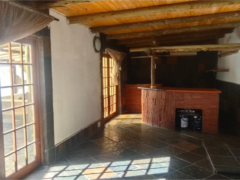 An indoor entertainment area featuring a built-in brick bar, slate tile flooring, and exposed timber ceiling beams with direct access to the patio.