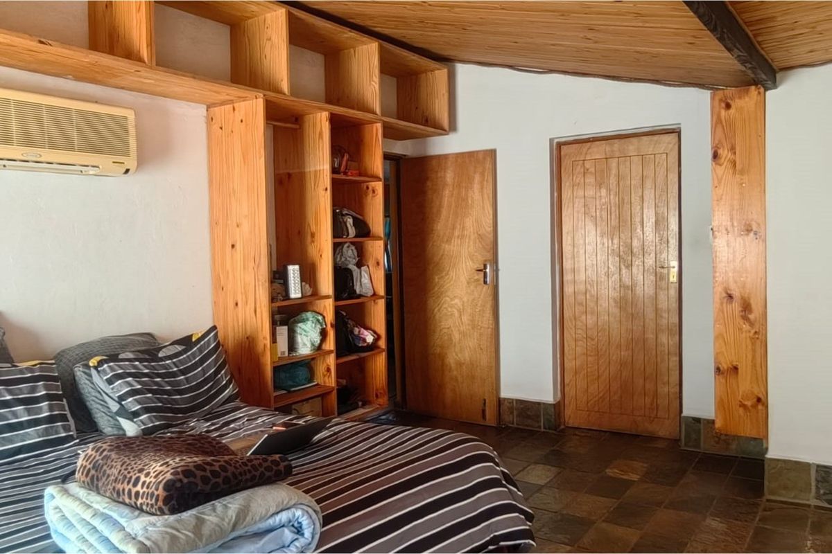 A bedroom featuring built-in wooden shelving, timber ceiling paneling, and slate-style floor tiles, providing a rustic aesthetic.