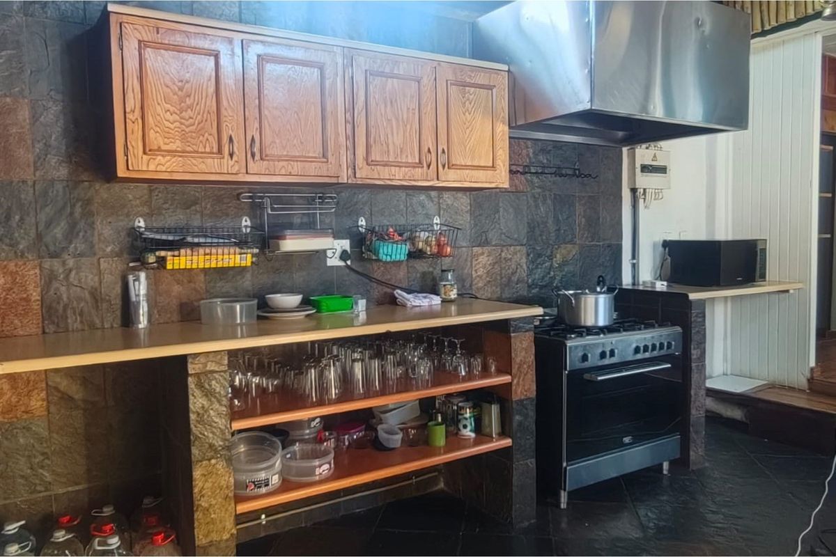 A functional kitchen area featuring dark stone wall tiling, wooden cabinetry, a freestanding stove with a stainless steel extractor hood, and open shelving.