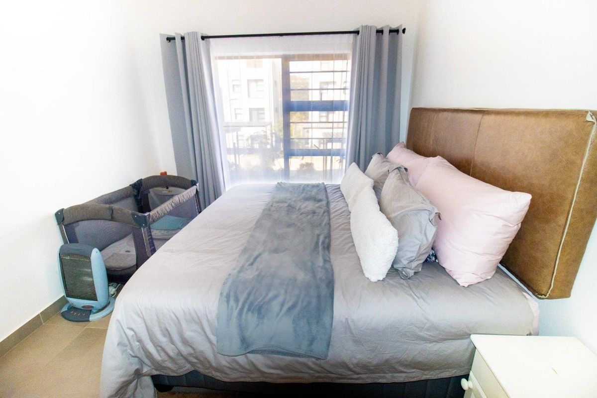 A well-lit bedroom featuring tiled flooring, a large window with curtain tracks, and neutral wall finishes.