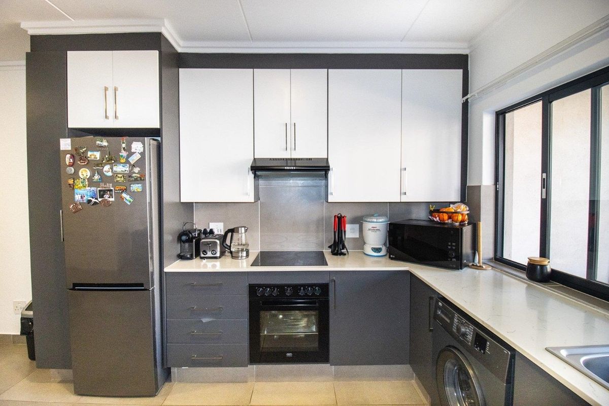 Modern kitchen featuring two-tone cabinetry, stone countertops, built-in oven, electric hob, extractor fan, and integrated space for a washing machine.