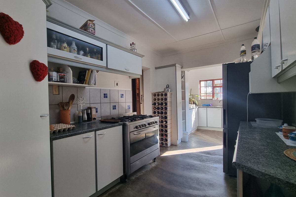 A functional kitchen featuring built-in cabinetry, a gas stove with oven, and tiled splashbacks, leading into a secondary prep or scullery area.