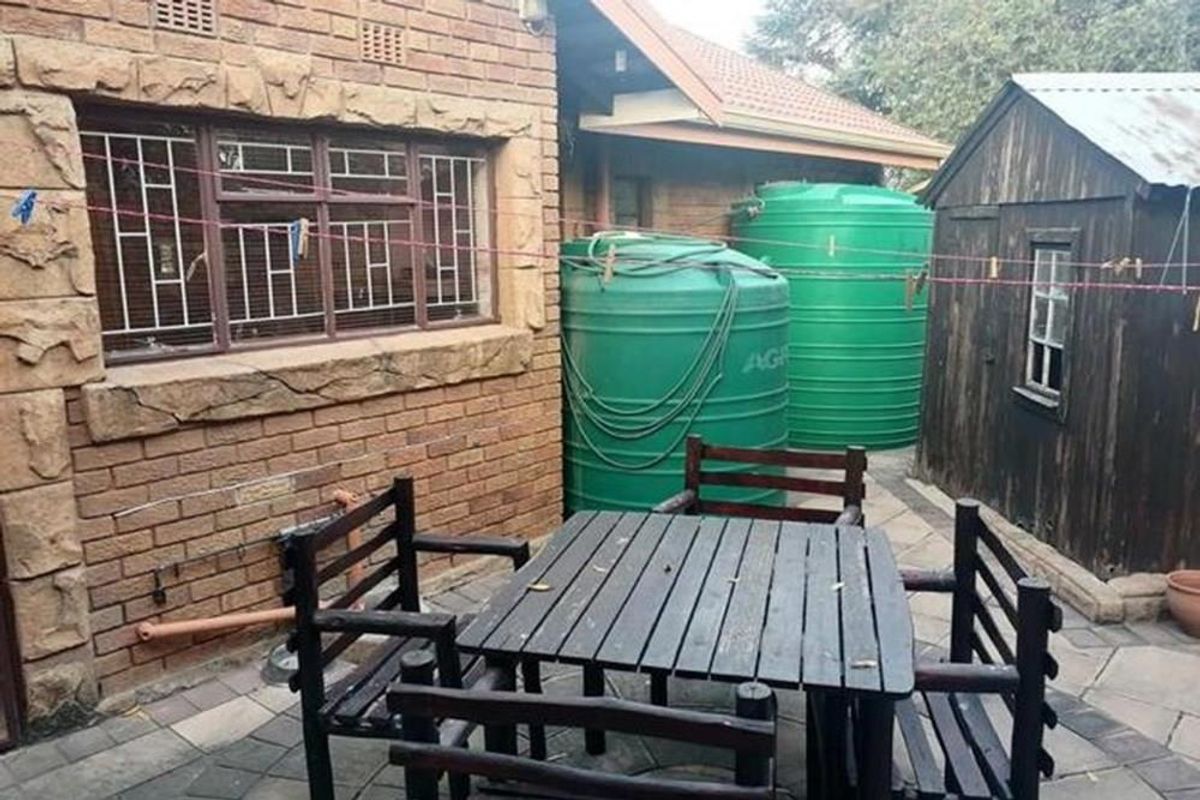 A rear exterior area featuring a paved patio, two large water storage tanks, and a detached timber storage shed adjacent to the main house.
