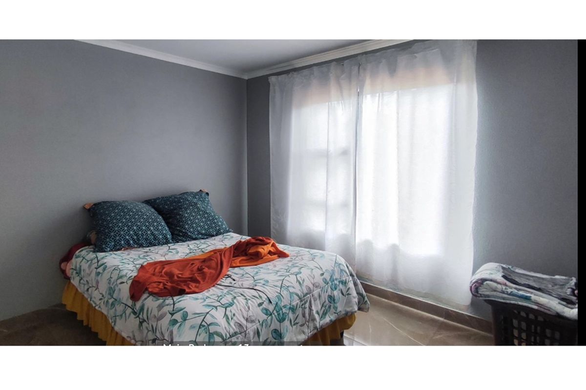 A bedroom featuring neutral grey walls, tiled flooring, and a large window with sheer curtains, providing natural light to the space.