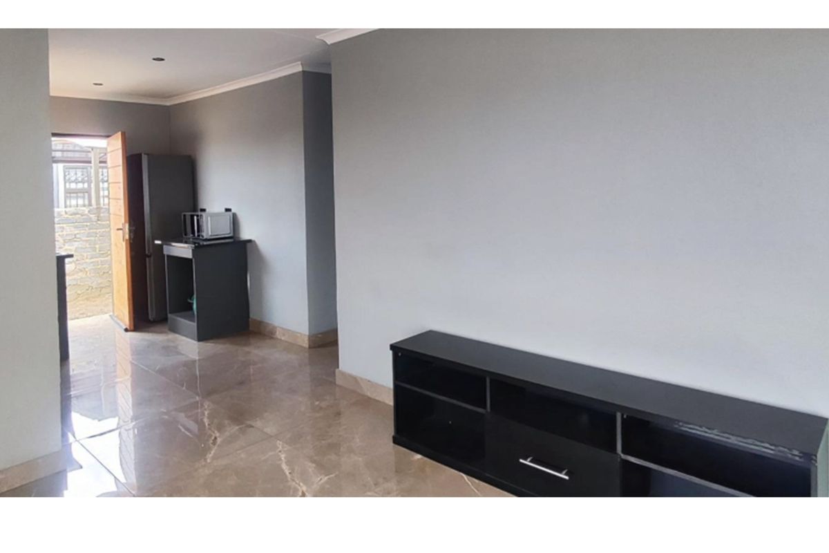 A living area featuring polished marble-look floor tiles, recessed ceiling lighting, and a neutral grey wall finish with direct access to the exterior.