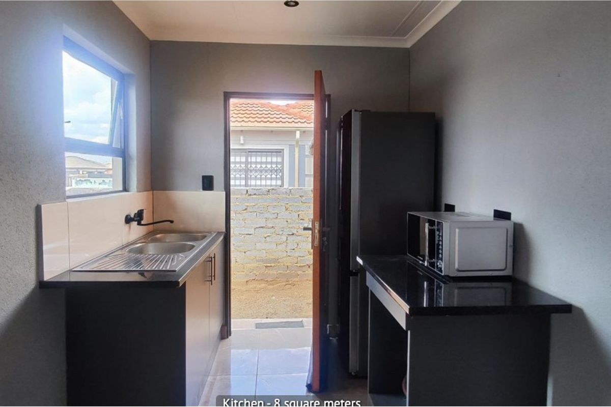 Compact kitchen featuring dark cabinetry, granite countertops, a double sink, and direct access to the rear exterior area.