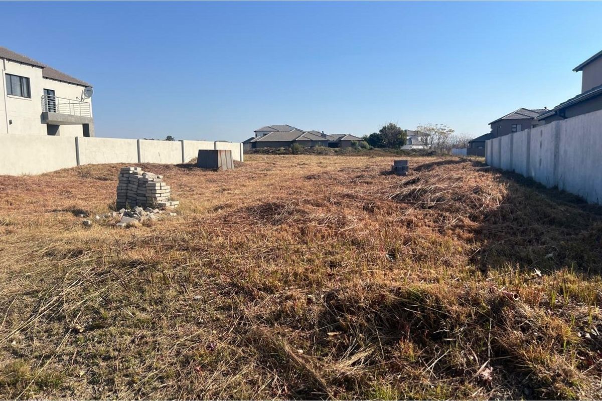 A vacant residential plot featuring perimeter boundary walls and natural grass coverage, situated within an established residential estate.
