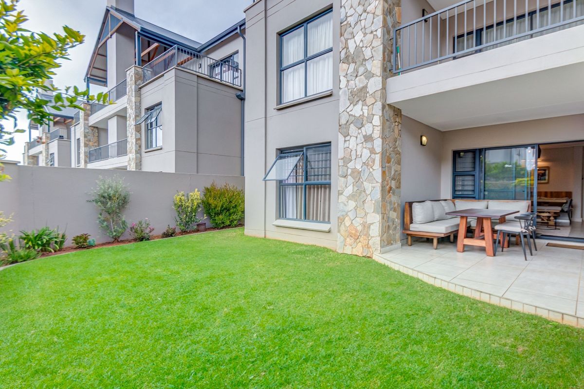 Rear view of the apartment building featuring a private garden, a tiled patio area, and stone-clad architectural detailing.