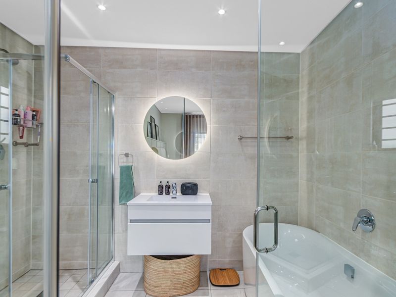 Modern bathroom featuring a walk-in glass shower, separate bathtub, wall-mounted vanity with basin, and a stylish backlit circular mirror.