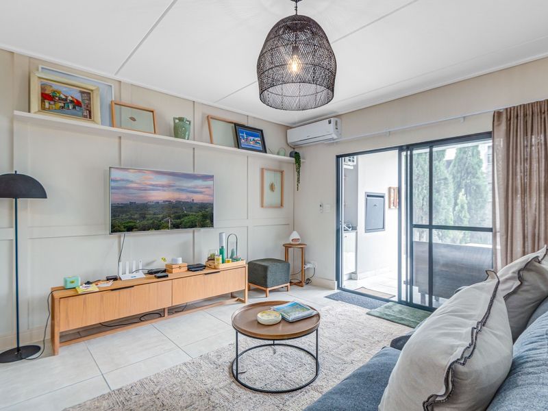 A well-maintained living room featuring decorative wall paneling, tiled floors, a split-system air conditioner, and direct access to an outdoor patio area.