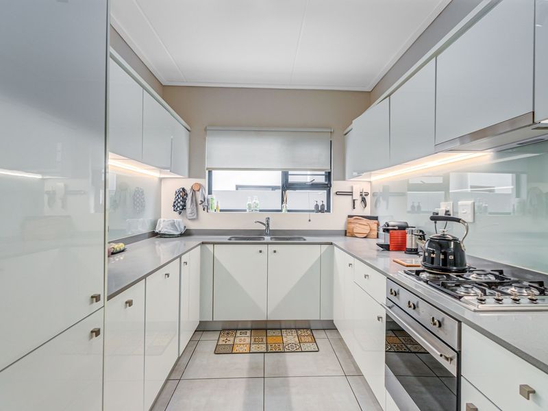 Modern galley-style kitchen featuring high-gloss cabinetry, stone countertops, integrated gas hob, oven, and under-cabinet lighting.