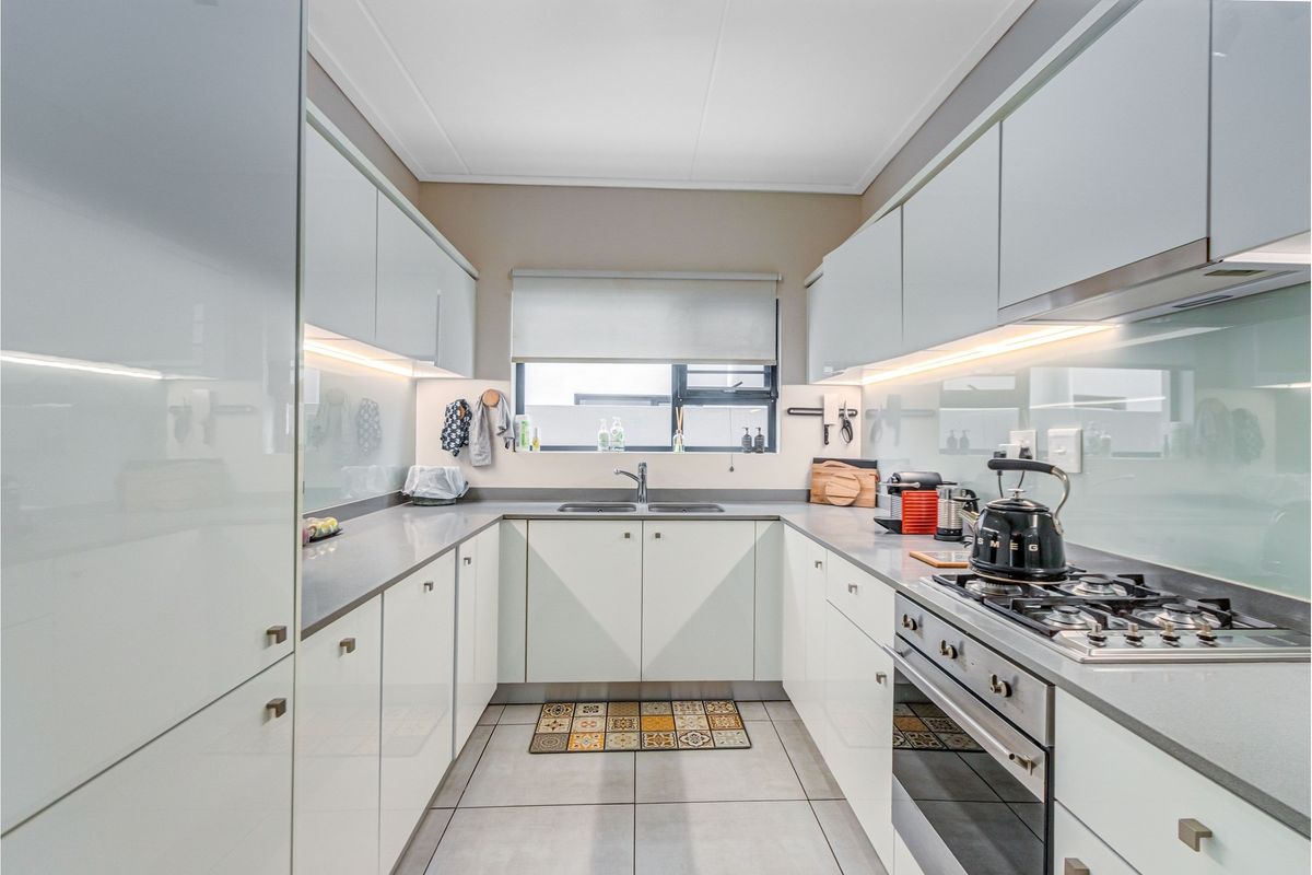 Modern galley-style kitchen featuring high-gloss cabinetry, stone countertops, integrated gas hob, oven, and under-cabinet lighting.