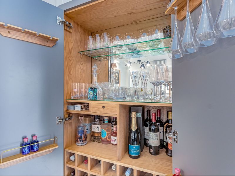 A custom-built integrated home bar cabinet featuring wooden shelving, a dedicated wine rack, mirrored backing, and built-in stemware storage.