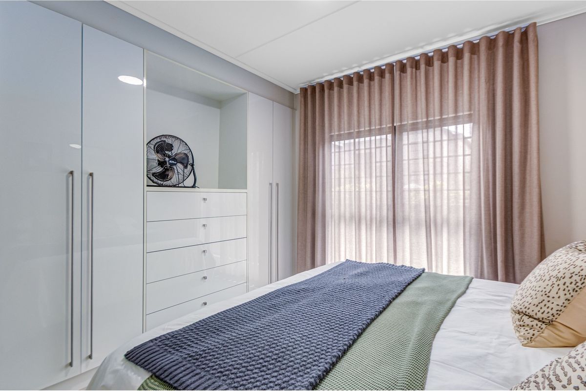 A well-maintained bedroom featuring modern high-gloss white built-in cupboards with integrated storage and neutral window treatments.
