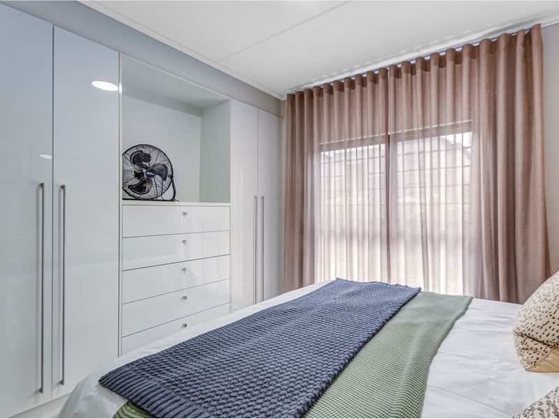 A well-maintained bedroom featuring modern high-gloss white built-in cupboards with integrated storage and neutral window treatments.