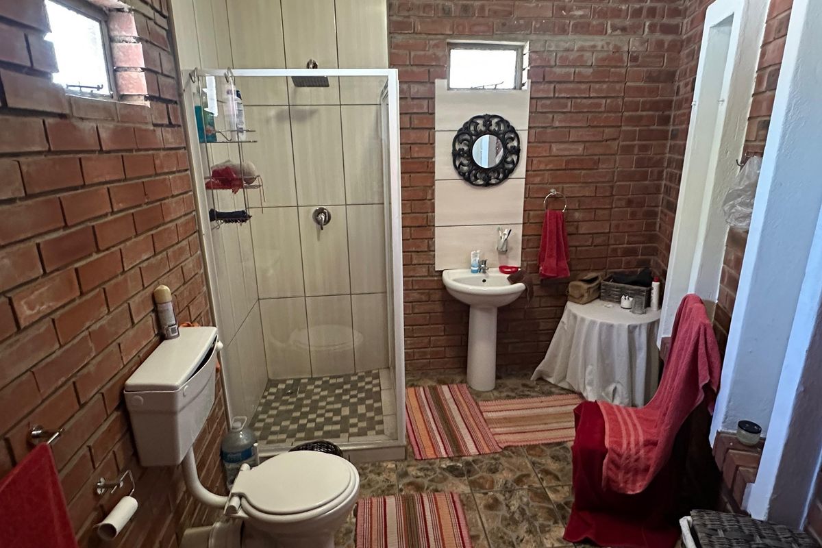 A bathroom featuring exposed brick walls, a pedestal basin, and a shower enclosure with tiled flooring.