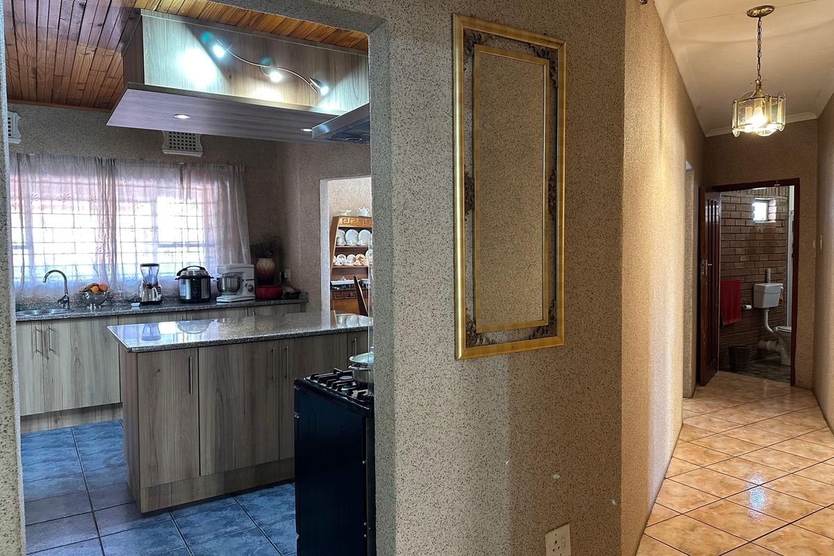 A functional kitchen featuring granite countertops, wood-look cabinetry, and a gas stove, seamlessly connected to a tiled hallway with warm lighting.