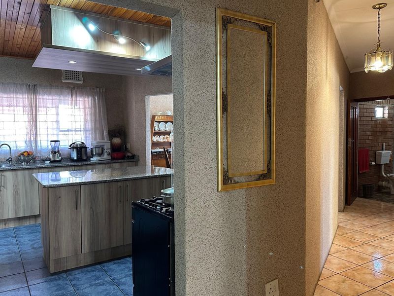 A functional kitchen featuring granite countertops, wood-look cabinetry, and a gas stove, seamlessly connected to a tiled hallway with warm lighting.