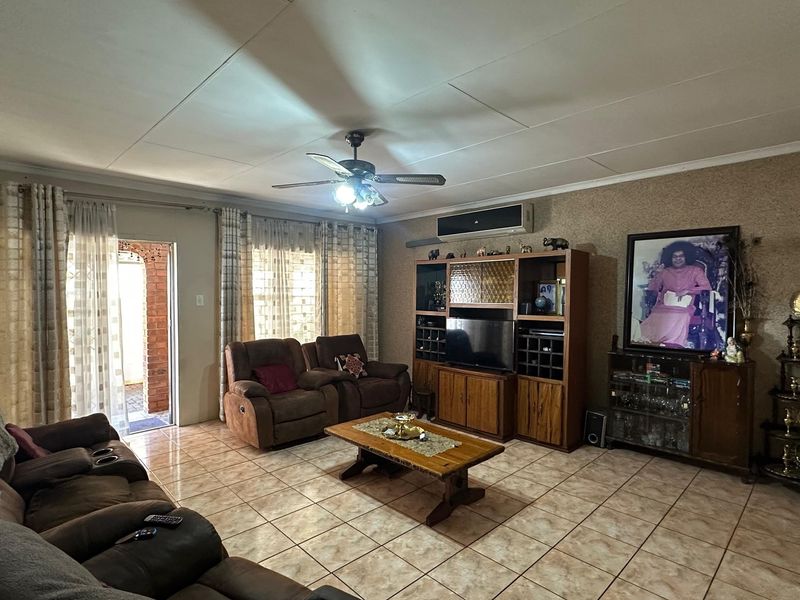 A spacious living room featuring tiled flooring, a ceiling fan, and a wall-mounted air conditioning unit, with direct access to an outdoor patio area.