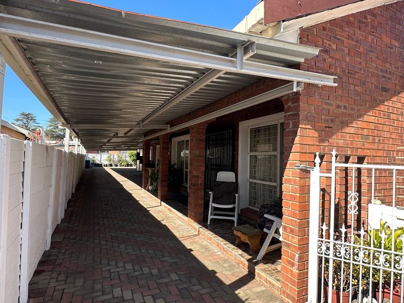 A brick-faced exterior featuring a long paved driveway covered by a corrugated metal carport and secured with metal gates.