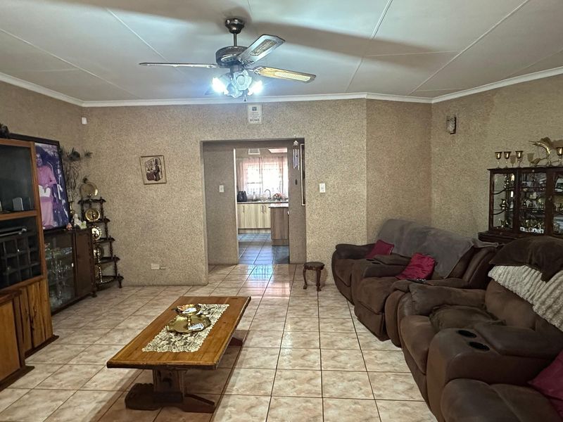 Spacious living room featuring tiled flooring, a ceiling fan, and an open archway leading through to the kitchen area.