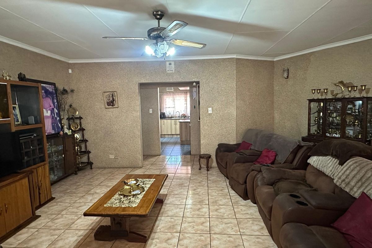 Spacious living room featuring tiled flooring, a ceiling fan, and an open archway leading through to the kitchen area.