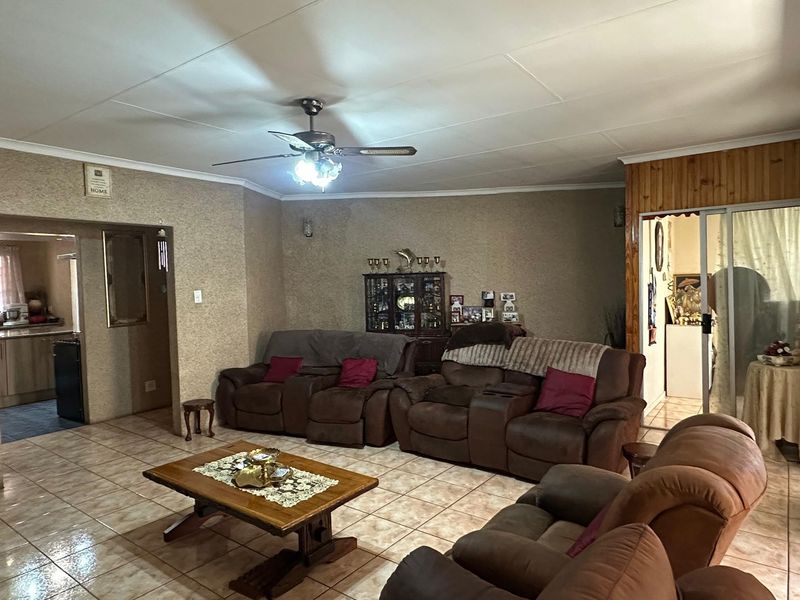 Spacious living room featuring tiled flooring, a ceiling fan, and wood paneling accents, with an open flow to the adjacent kitchen area.