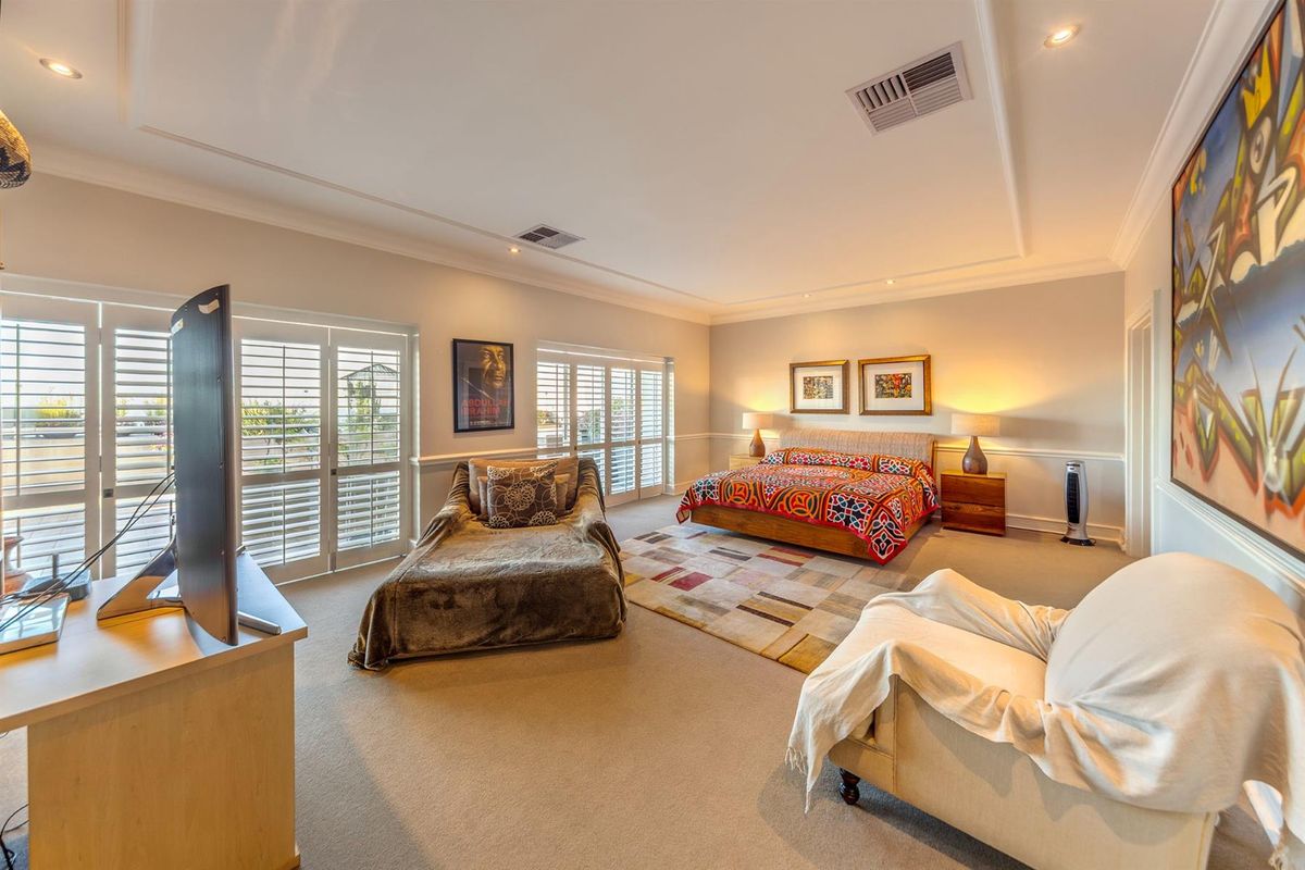 Spacious bedroom featuring recessed ceiling lighting, ducted air conditioning, and plantation shutters opening to a balcony area.