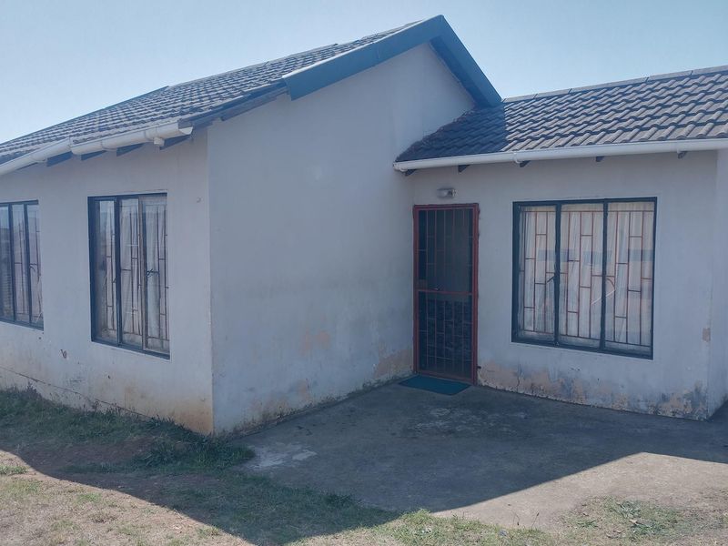 Front view of a single-story house featuring a tiled roof, security gate, and concrete patio area with visible exterior wall maintenance required.