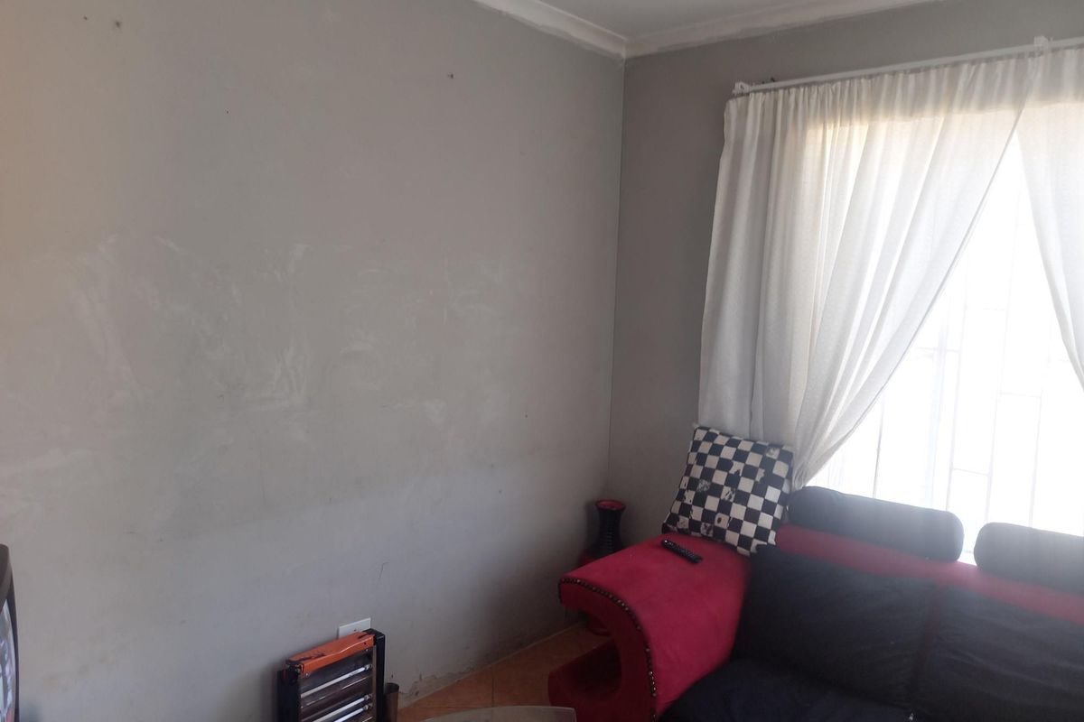 A living room area featuring a window with security bars and curtain rails, showing signs of wear on the wall surfaces.
