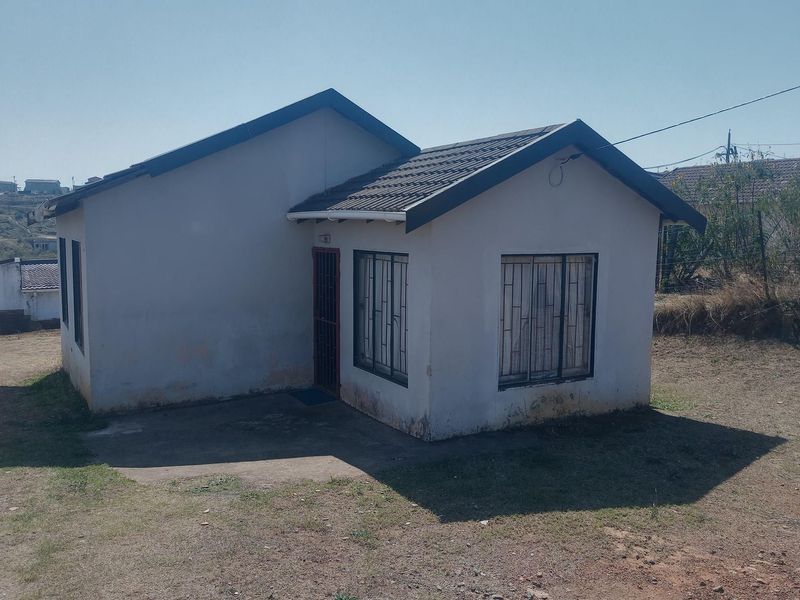 A detached single-story house featuring a tiled roof, security bars on windows, and a concrete entrance area, set on a large plot.